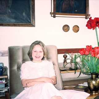Young girl in white dress smiling indoors near flowers.