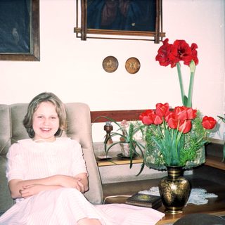 Young girl in white dress smiling indoors near flowers.