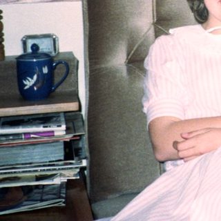 Young girl in white dress smiling indoors near flowers.