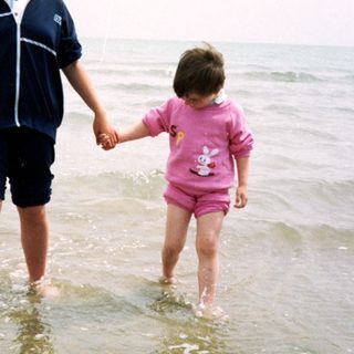 Two children holding hands walking in shallow ocean water.