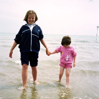 Two children holding hands walking in shallow ocean water.