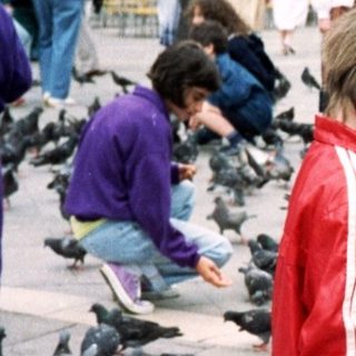 Child feeding pigeons in historic city square.