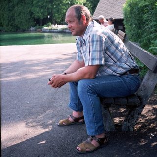 Man sitting alone on park bench near water.