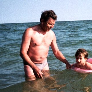 Shallow water scene: man assisting young child swimming.