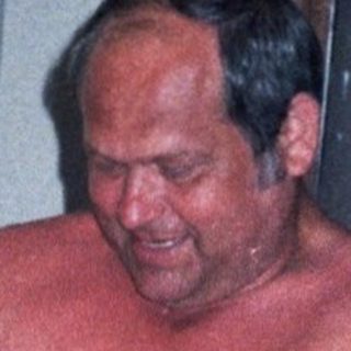 Shirtless man sitting on chair with child nearby.