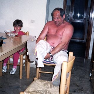 Shirtless man sitting on chair with child nearby.