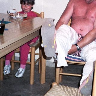 Shirtless man sitting on chair with child nearby.