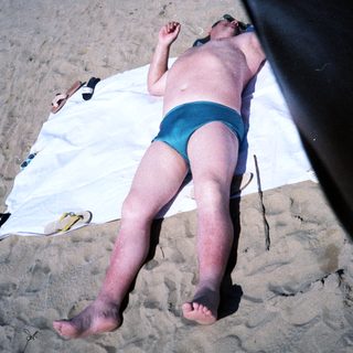 Person sunbathing on beach towel in swim trunks.