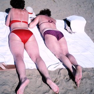 Two women mid-air on beach towels.