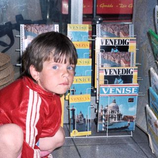 Child in red outfit kneeling near Venice postcards.
