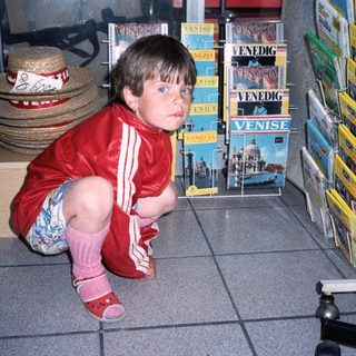 Child in red outfit kneeling near Venice postcards.