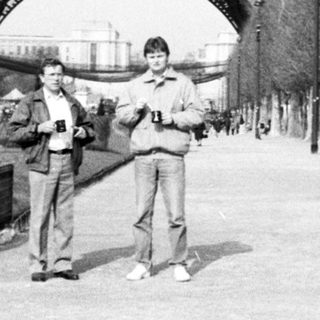 Two men posing near Eiffel Tower entrance.