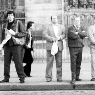Group of men posing outside Gothic cathedral façade.