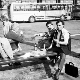 Three men sitting on bench drinking outdoors near buses.