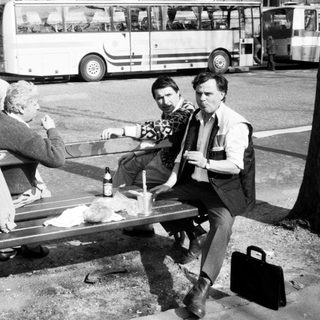 Three men sitting on bench drinking outdoors near buses.