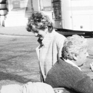 Three men sitting on bench drinking outdoors near buses.