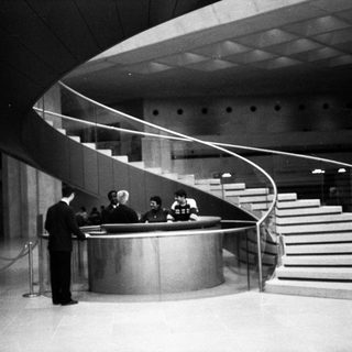 Modernist building lobby with curved staircase and reception desk.