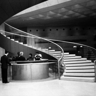 Modernist building lobby with curved staircase and reception desk.