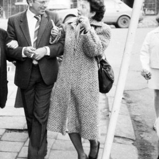 Group of people walking outdoors in 1960s-70s attire.