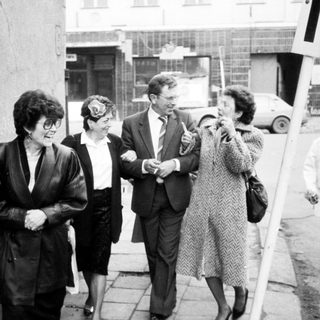 Group of people walking outdoors in 1960s-70s attire.