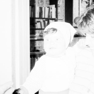Child brushing teeth indoors near bookshelf.