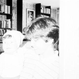 Child brushing teeth indoors near bookshelf.