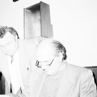 Two men examining a modern geometric sculpture indoors.