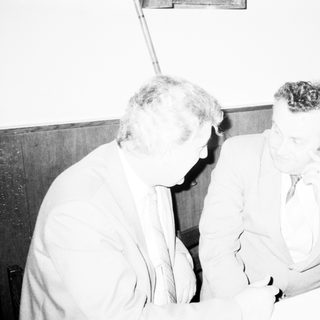 Two men engaged in serious conversation indoors.