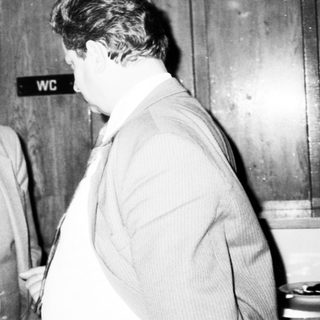 Three men in formal attire conversing indoors near restrooms.
