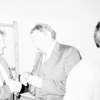 Two men exchanging a small object formally.