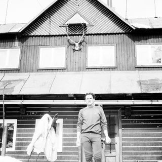 Man standing outside snowy wooden house.