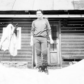 Man standing outside snowy wooden house.