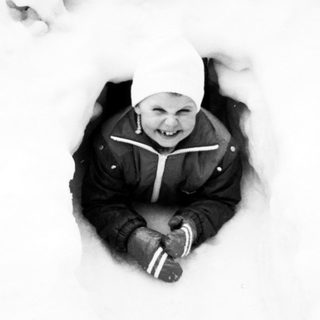 Child buried in snow, smiling happily.