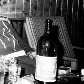 Two people sitting indoors, appearing relaxed with wine bottle.