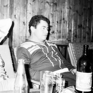 Two people sitting indoors, appearing relaxed with wine bottle.