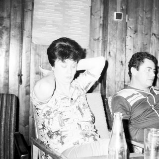 Two people sitting indoors, appearing relaxed with wine bottle.