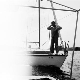 Person standing on sailboat adjusting sail.