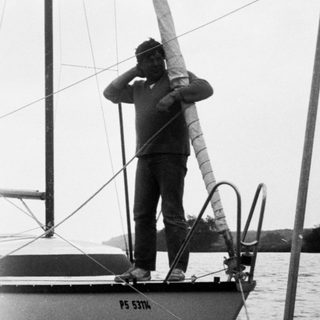 Person standing on sailboat adjusting sail.