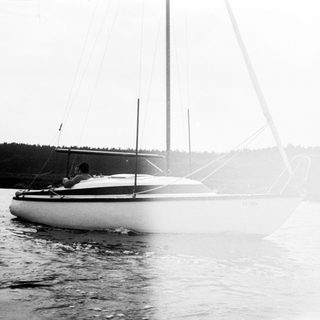 Sailboat gliding on calm water with person aboard.