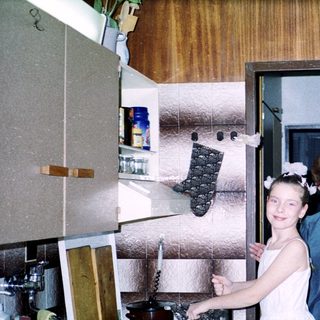 Two women in kitchen: young girl in bridesmaid dress with older woman.