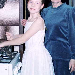 Two women in kitchen: young girl in bridesmaid dress with older woman.