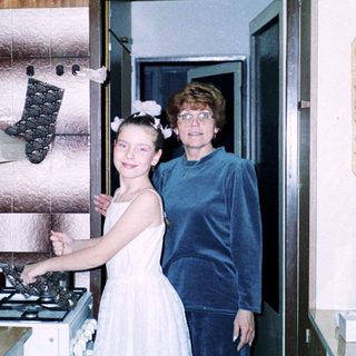 Two women in kitchen: young girl in bridesmaid dress with older woman.
