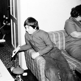 Two children playing video game with adult nearby.