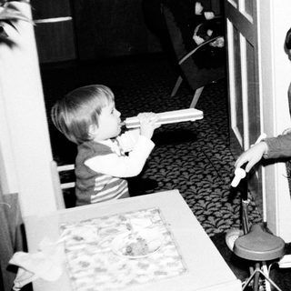 Two children playing video game with adult nearby.