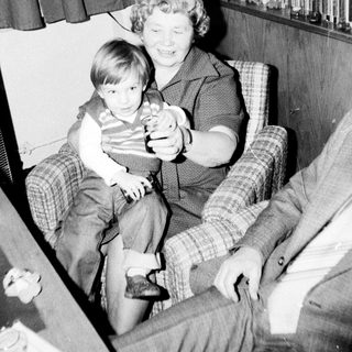 Woman holding young child indoors with toy.