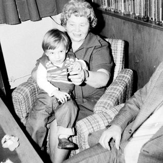 Woman holding young child indoors with toy.
