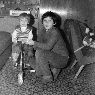 Two children playing with a tricycle indoors.