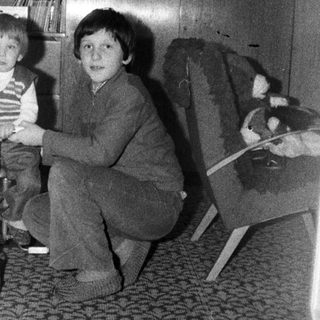 Two children playing with a tricycle indoors.