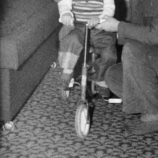 Two children playing with a tricycle indoors.