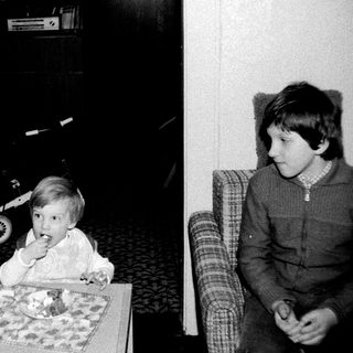 Two children eating cake indoors, one seated at table.